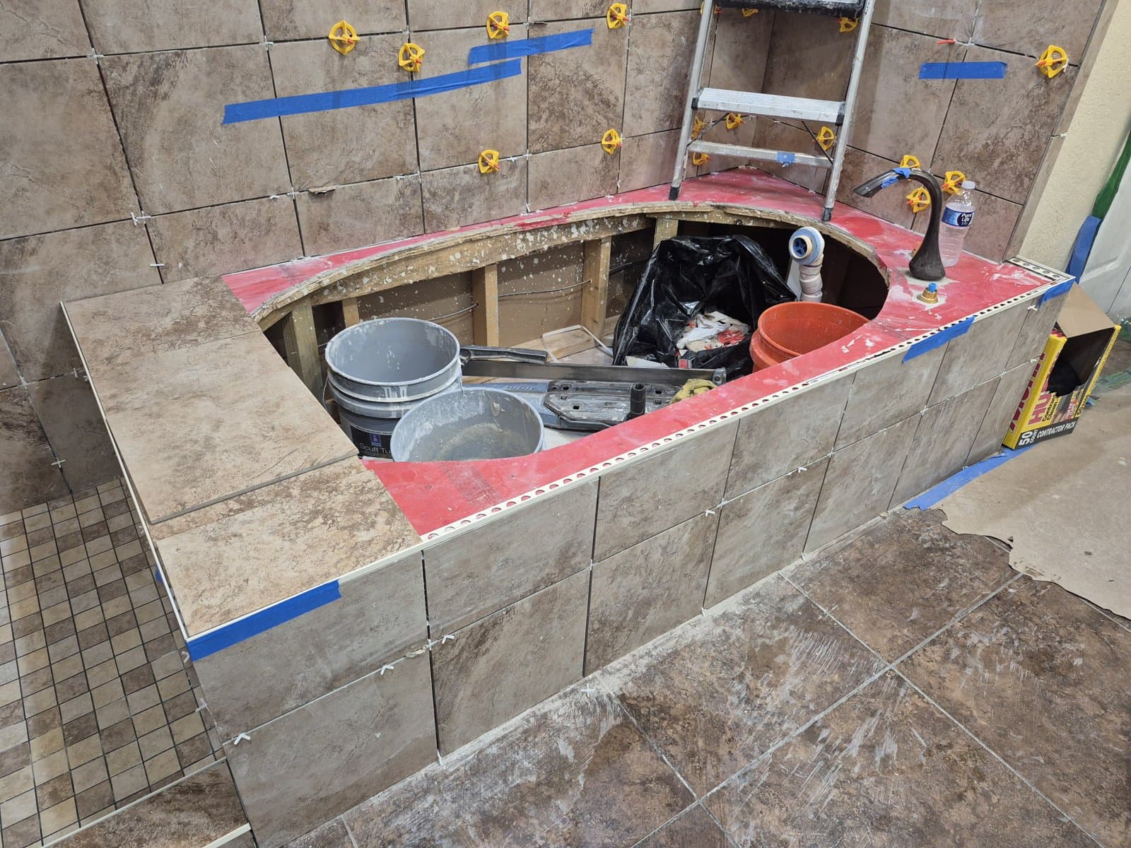 Waterproofing in progress on a San Antonio bathroom by Raging Bull Contracting — red waterproofing membrane over a tub deck with large-format tile being set over it using leveling clips