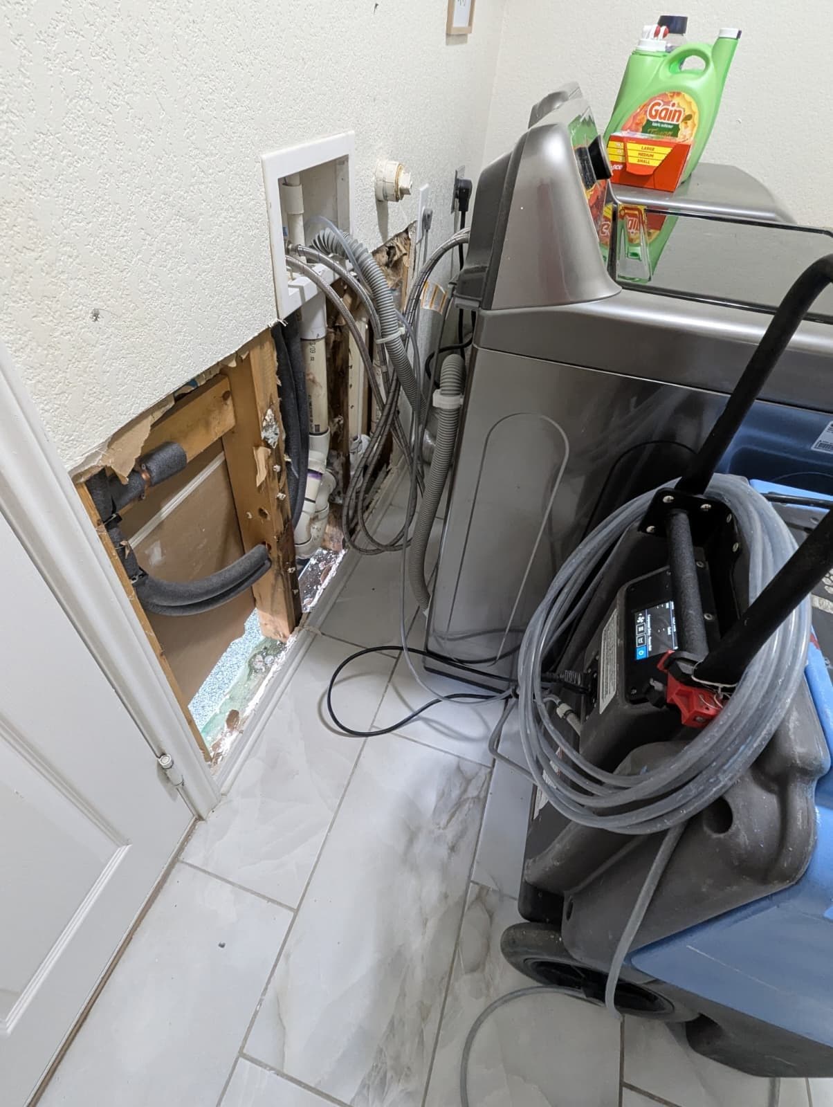 Laundry room wall opened below the washer box in Cibolo, exposing wet drywall edge, framing and plumbing lines